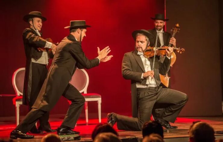un cuarteto de músicos sobre el escenario, uno tocando el violín y los otros animándole y aplaudiendo