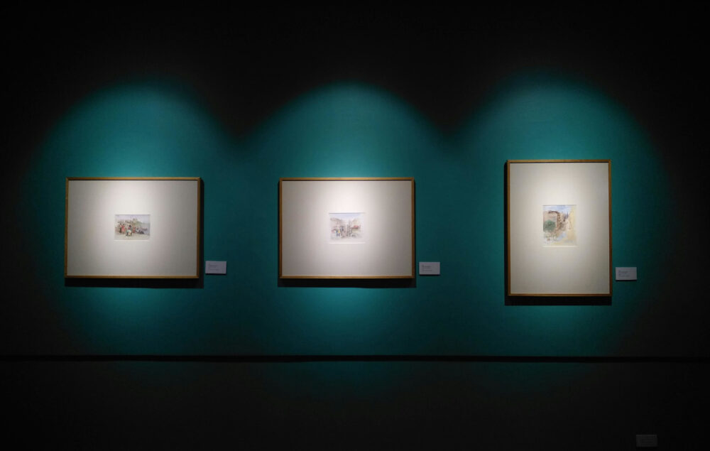 Tres marcos con una foto cada una sobre pared azul verdosa a modo de sala de exposiciones