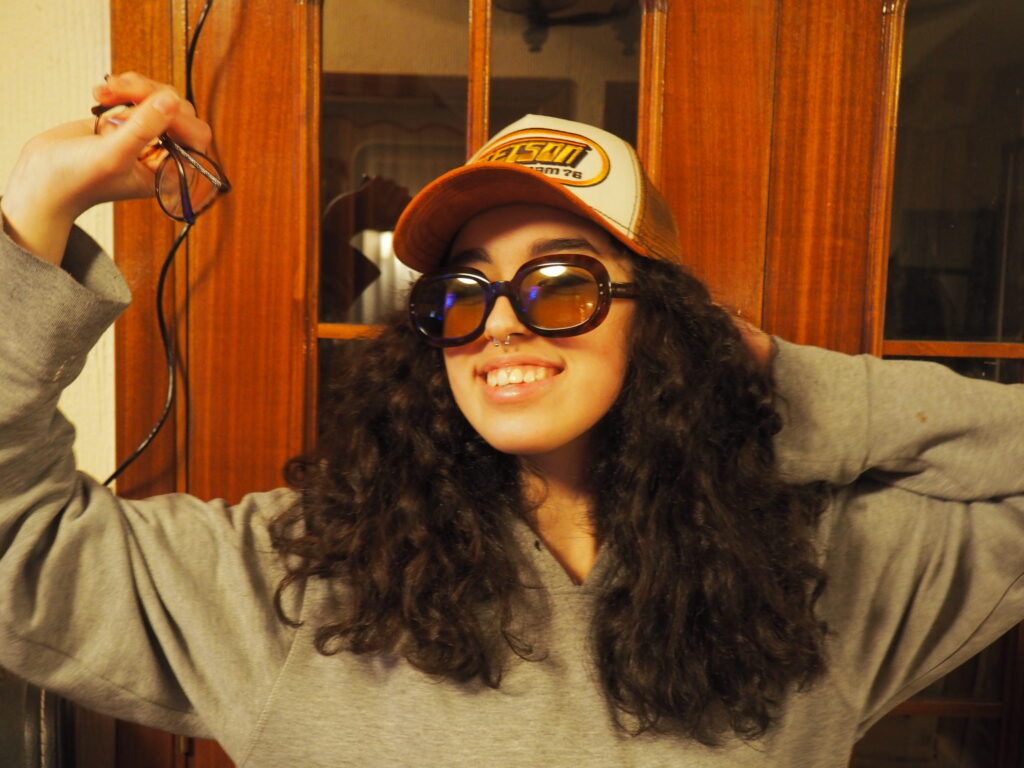 Imagen de Claudia Pumarega en la que se ve una chica joven de rizos con una gorra y gafas de sol