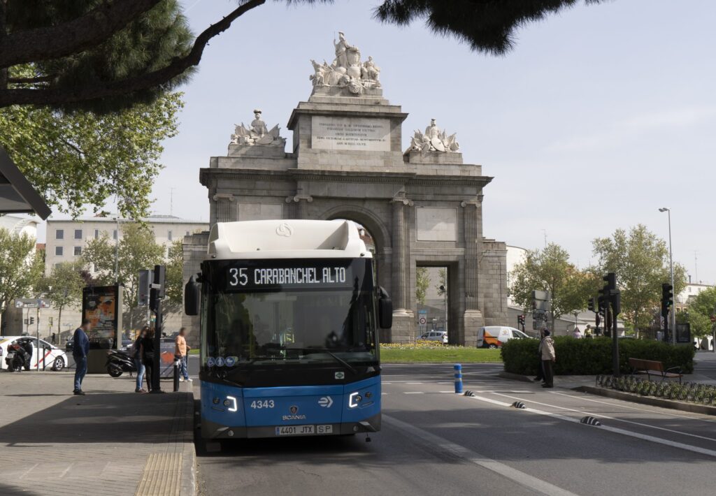 Un autobús con la puerta de alcalá de fondo