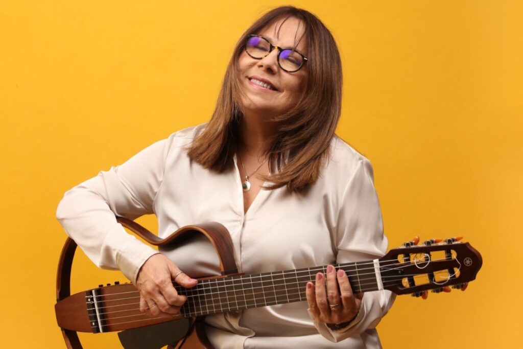 Una mujer tocando la guitarra con fondo amarillo detrás
