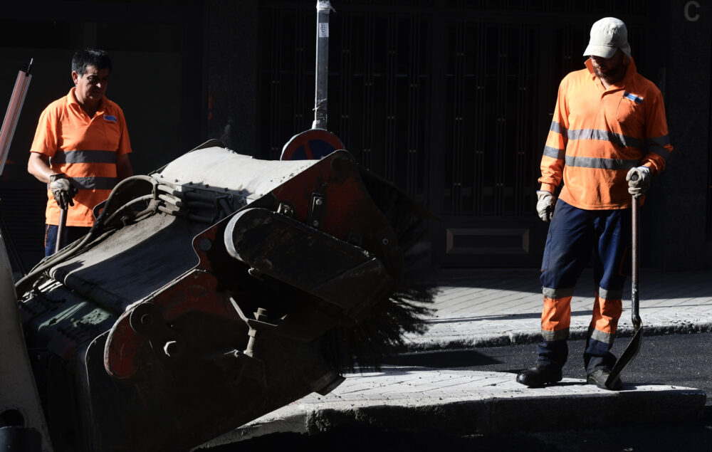 Dos operarios trabajando en la Operación Asfalto con chalecos reflectantes y herramientas de obra