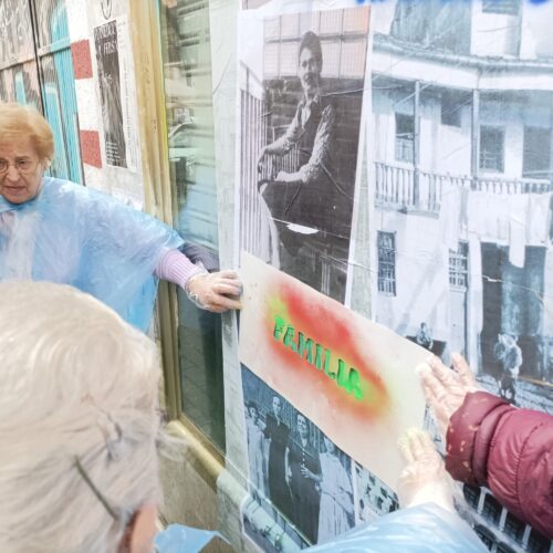 una señora mayor sujetando una plantilla mientras otras personas hacen el graffiti