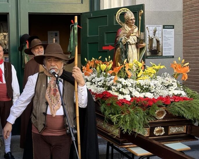 Cofrade e imagen de san Blas sobre su trono adornado de flores de colores