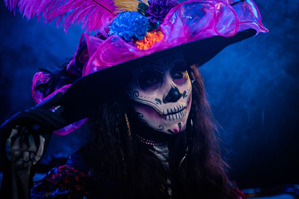 Mujer con sombrero y cara pintada en blanco simulando una calavera