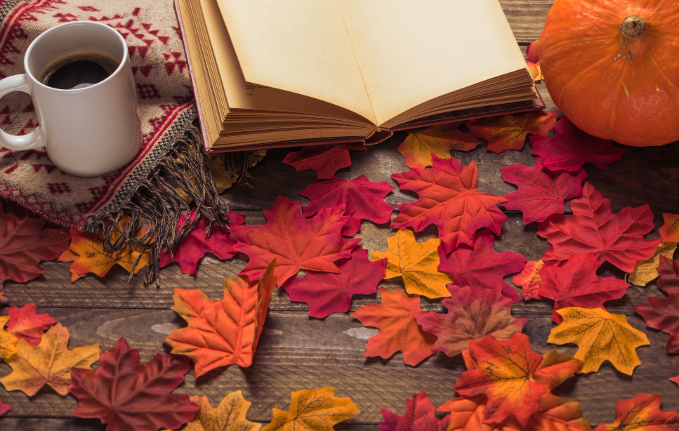 Imagen con un libro y hojas de otoño sobre una mesa