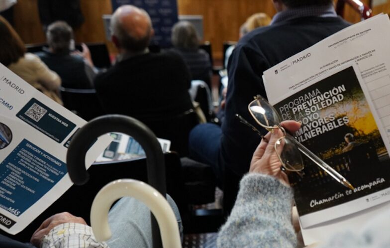 Un grupo de personas mayores sentadas en las gradas de un auditorio sujetando los folletos