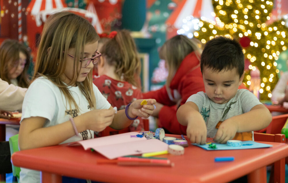 Unos niños haciendo manualidades sobre una mesa infantil con decoración navideña