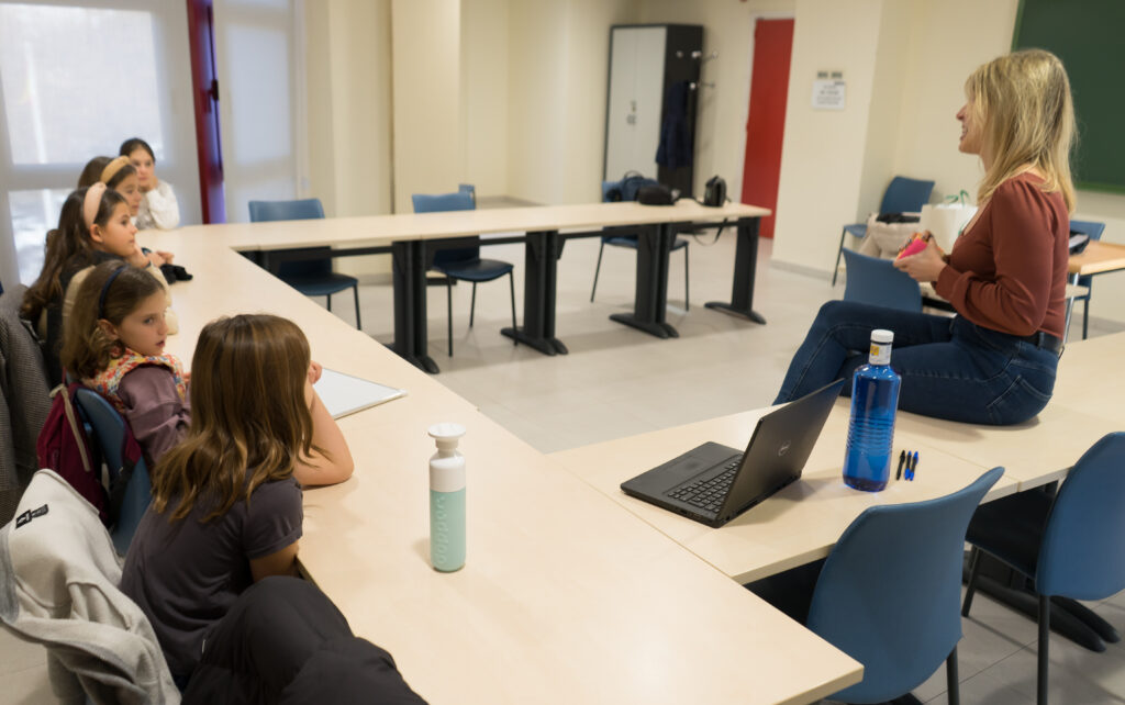 Un grupo de niñas en un aula atendiendo a su mentora en el aula donde están desarrollando sus proyectos de emprendimiento