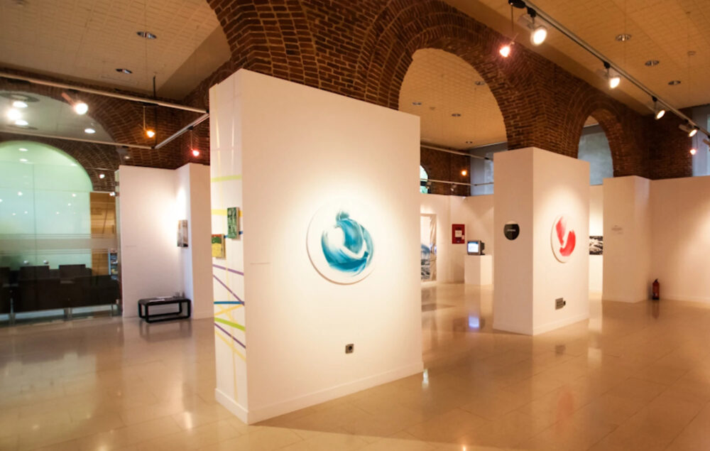 Imagen destacada para ilustrar el post sobre qué hacer el fin de semana en Chamberí donde se muestra la sala de exposiciones con paneles blancos, obras de arte contemporáneo y arcos de ladrillo visto iluminados por focos.