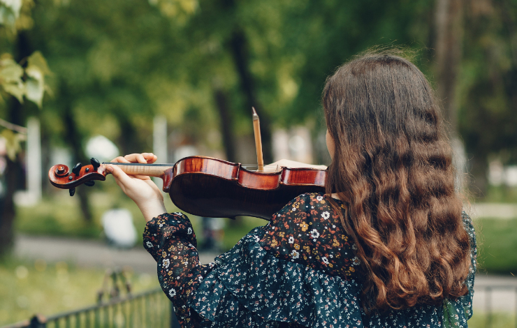 Foto de espaldas de una artista femenina tocando el violín en un parque