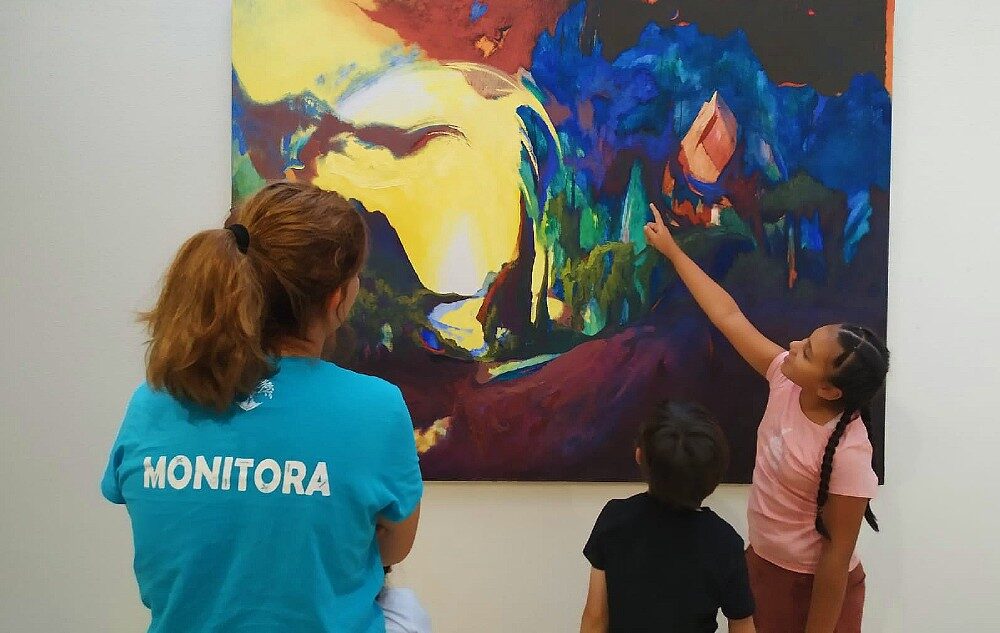 Monitora del servicio de ludotecas de Latina con un niño y una niña ante un cuadro