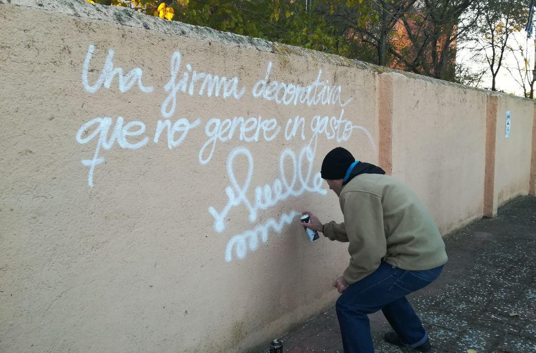 Escritor de grafiti plasmando la frase de Muelle en el muro