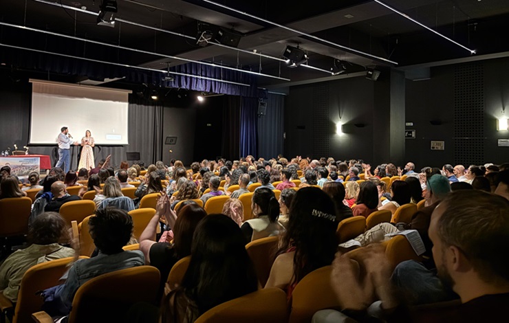 Auditorio lleno de participantes en las I Jornadas de servicios sociales. Sobre el escenario hablan el concejal del Puente de Vallecas y la jefa de servicios sociales del distrito