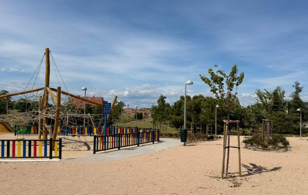 Parque con una zona de columpios y juegos infantiles con suelo de arena