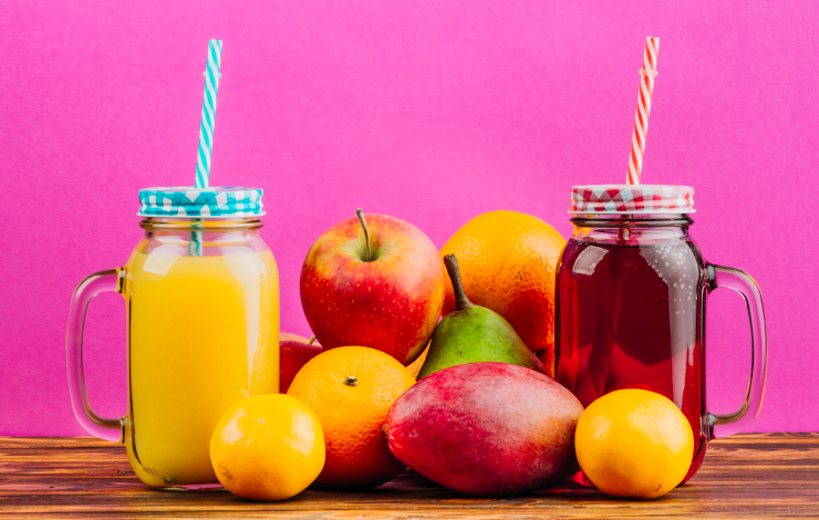 Foto de bodegón de zumos naturales de fruta en dos envases transparentes con pajita y varias piezas de fruta entre medias