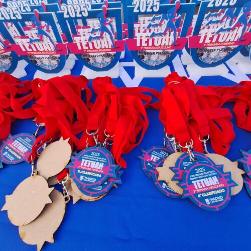 Medallas y trofeos del Cross escolar de Tetuán 2025 sobre una mesa azul