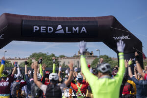 ciclistas de espaldas levantando los brazos justo antes de salir de la meta, imagen del Madrid to Barcelona 2024