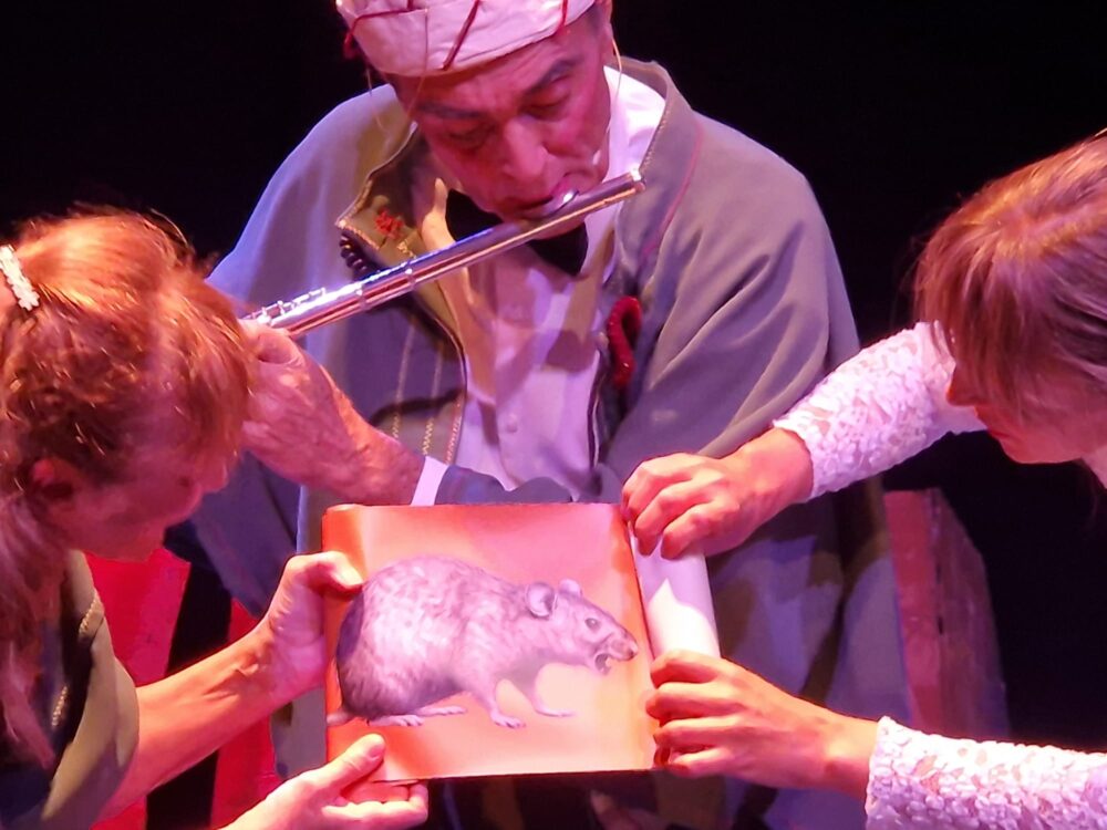 Escena del flautista de Hamelin con dos mujeres y la imagen de una rata