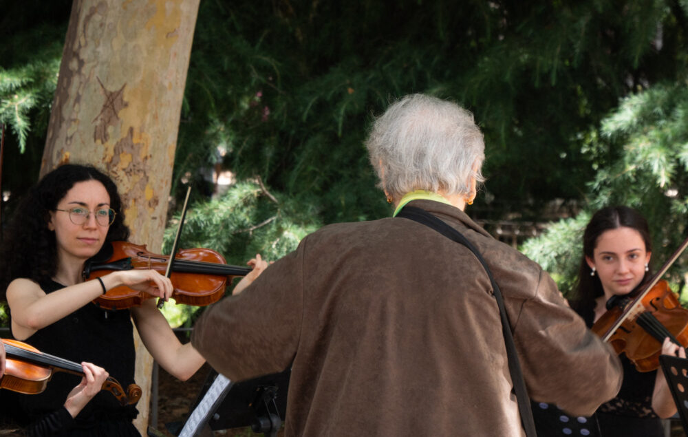 Una mujer frente a dos chicas con violines de una orquesta