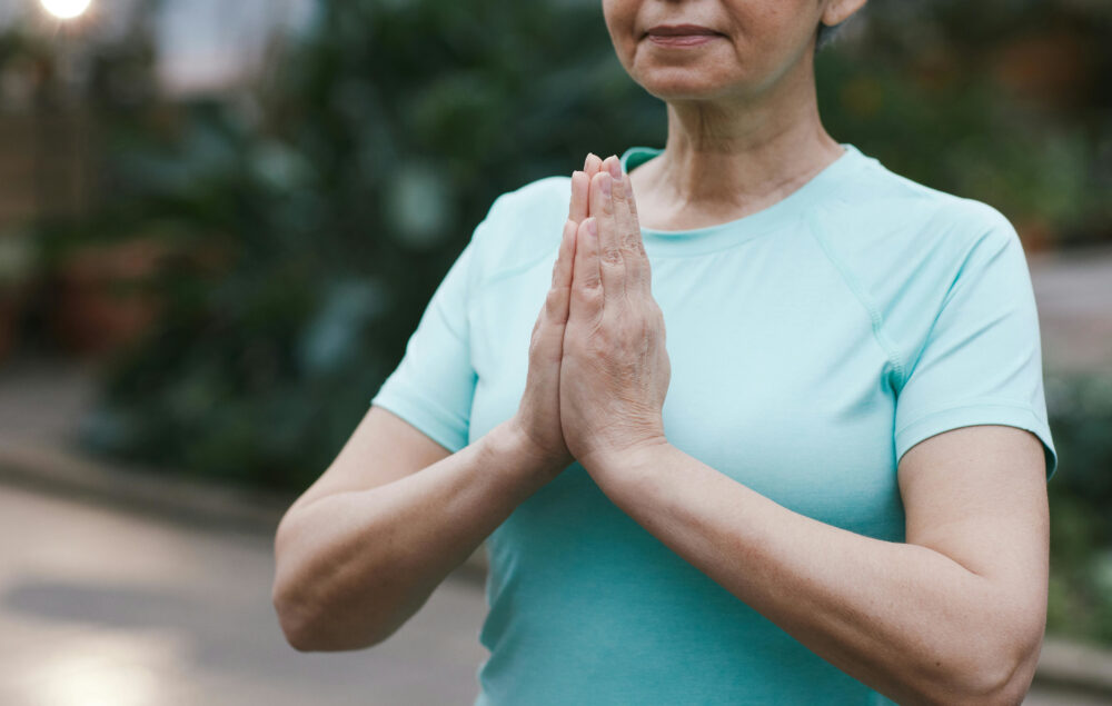 Imagen de una mujer mayor con una camiseta azul de manga corta haciendo yoga