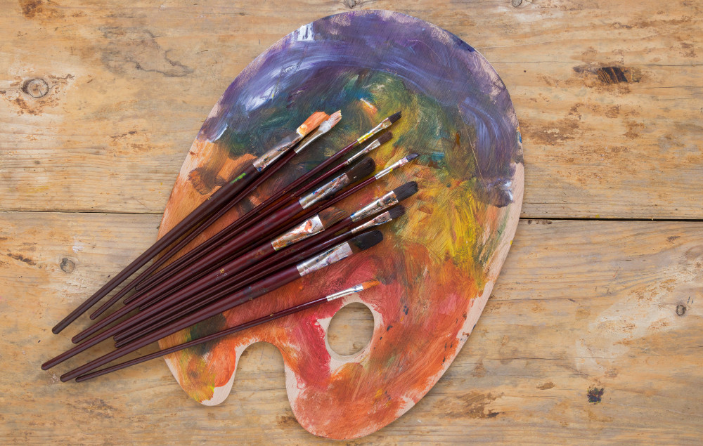 Una paleta de pinturas con pinceles encima sobre una tabla de madera