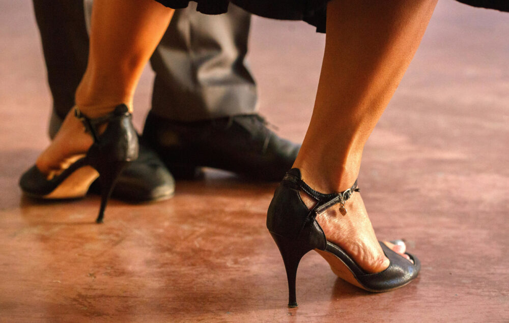 imagen de dos personas bailando y se ven unos tacones y unos zapatos de baile negros