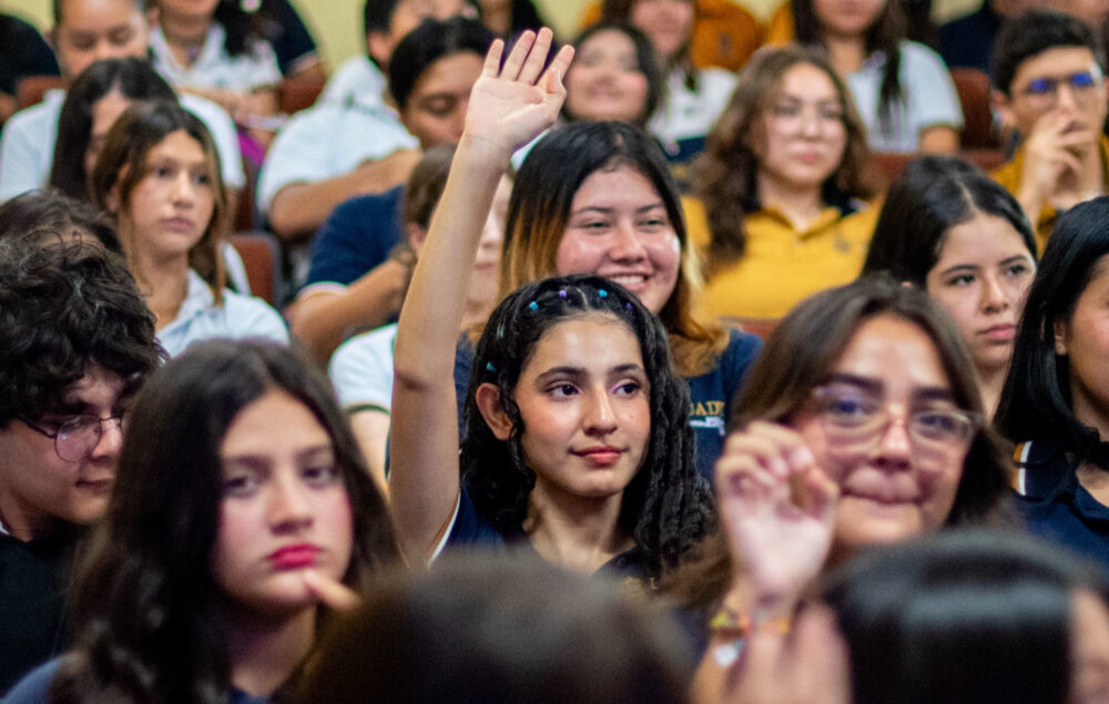 Una chica joven levanta el brazo para participar entre el público de una charla