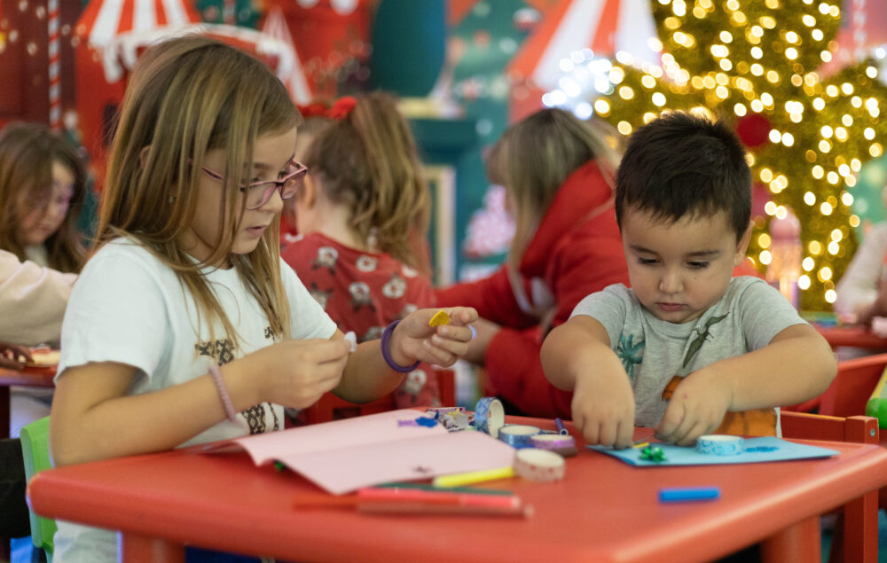 Niños haciendo actividades en una mesa de un colegio con decoración navideña de fondo
