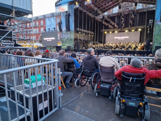 Personas en silla de ruedas siguen un concierto en una zona adaptada a sus capacidades de movilidad