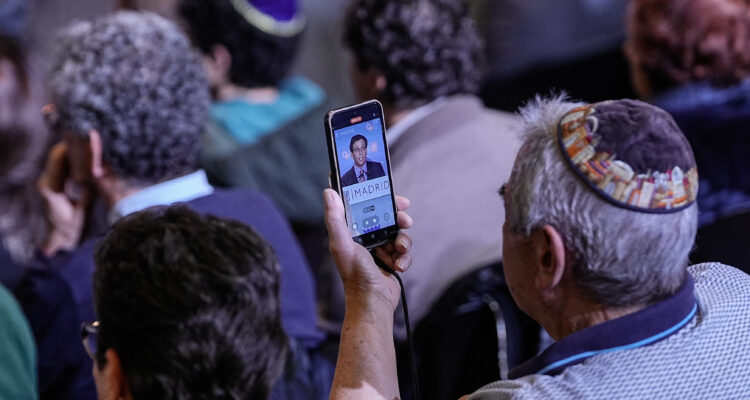 Un asistente a la Janucá mientras graba con el móvil al alcalde, José Luis Martínez-Almeida