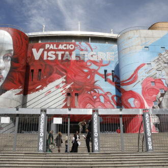 Imagen del mural en la fachada del Palacio de Vistalegre que se ve una mujer con pelo rojo tocando una guitarra