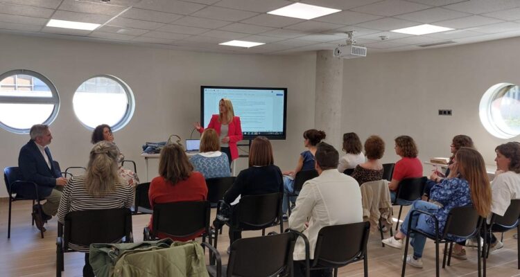 Una mujer dando unas palabras frente a un grupo de personas en una sala dónde se desarrolla el programa 'Camino al empleo'