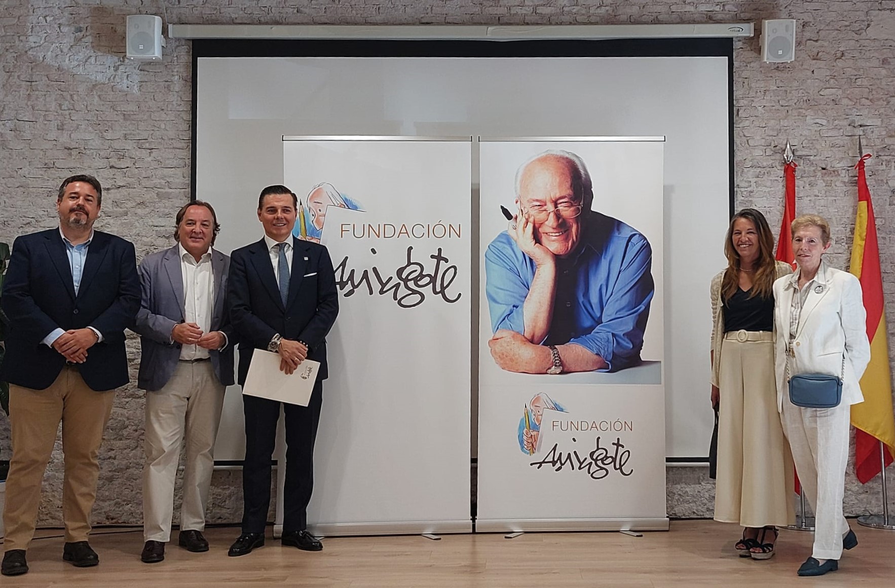 Imagen de seis personas posando frente a dos carteles de la Fundación Antonio Mingote, uno de ellos con la fotografía de un hombre mayor sonriendo. 