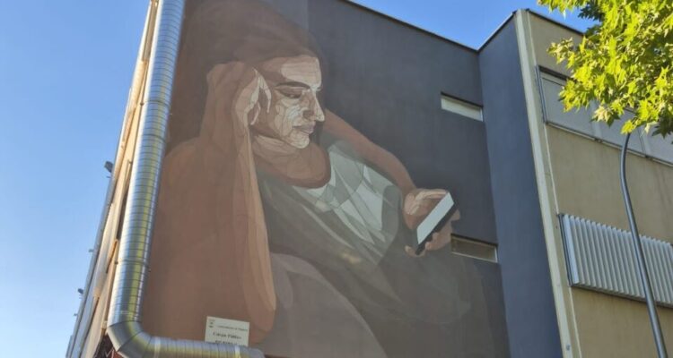 Mural de la chica apoyada en su codo leyendo un móvil