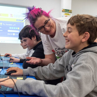 Una mujer ayudando a unos niños con ordenadores