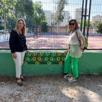 dos mujeres con un mural de fondo de la IDB San Juan Bautista-Cidamón