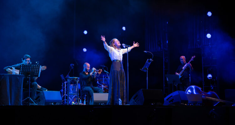 Una emocionada Mónica Molina en el escenario del Centro de Cultura Contemporánea Conde Duque, con los brazos abiertos y de pie, con algunos miembros de la banda de fondo
