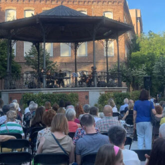 Concierto del ciclo 'Chamberí en Clave de Sol' en la plaza de Chamberí, con el público sentado y la banda tocando en el templete