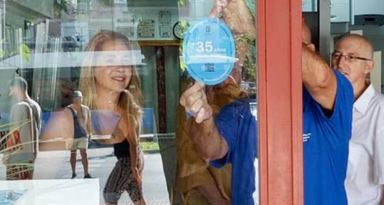 Un hombre colocando el distintivo 'Treintañero de Ciudad Lineal' en el escaparate de uno de los locales reconocidos