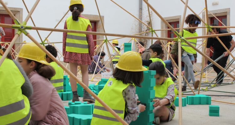 Unos niños haciendo manualidades con una construcción con chalecos amarillos