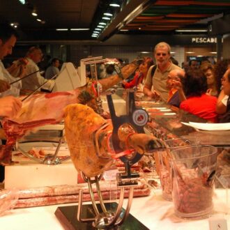 Trabajadores del sector servicios cortan jamón en un mercado durante su jornada laboral en Madrid