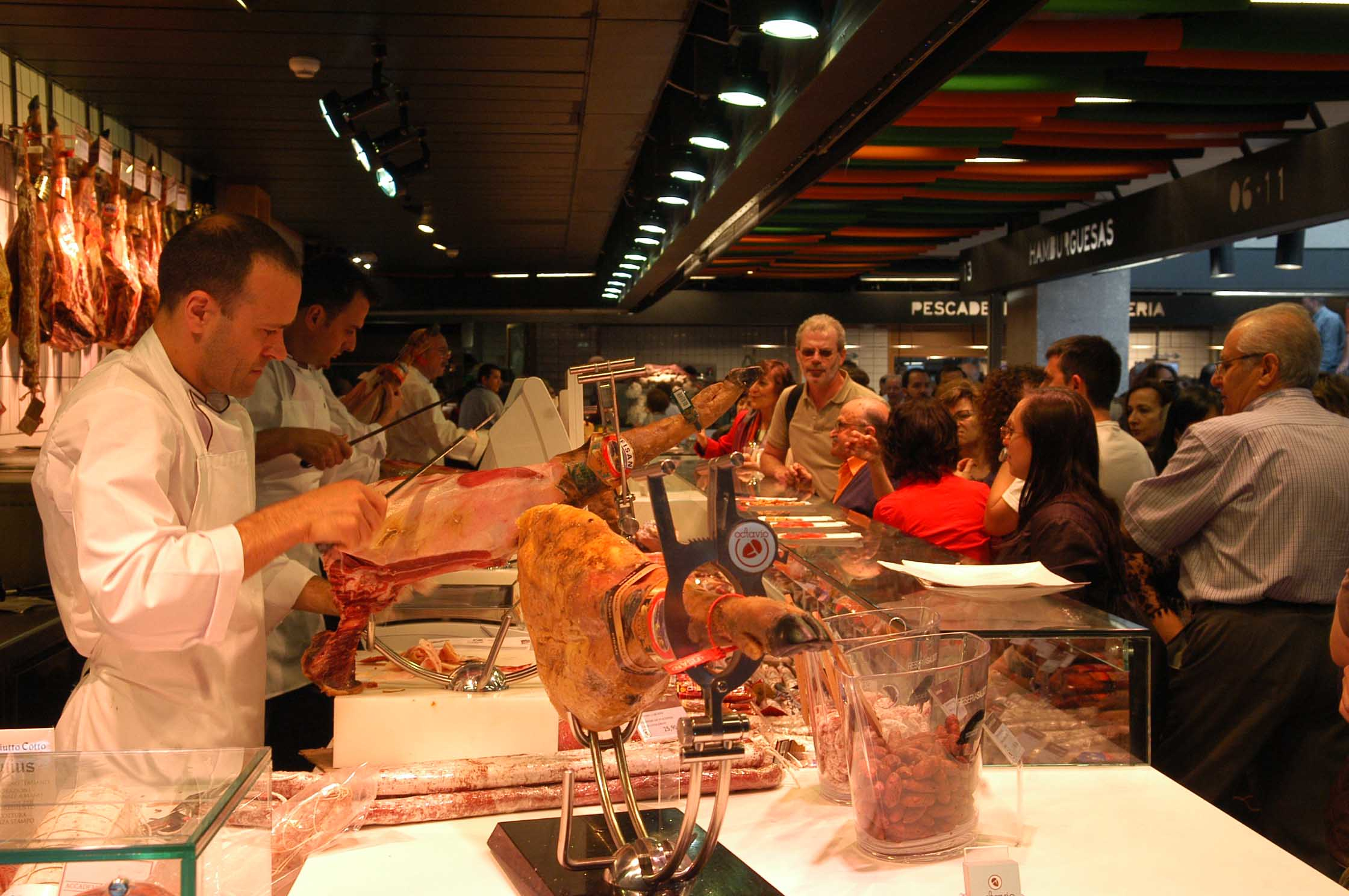 Un trabajador del sector servicios corta jamón en un mercado durante su jornada laboral en Madrid