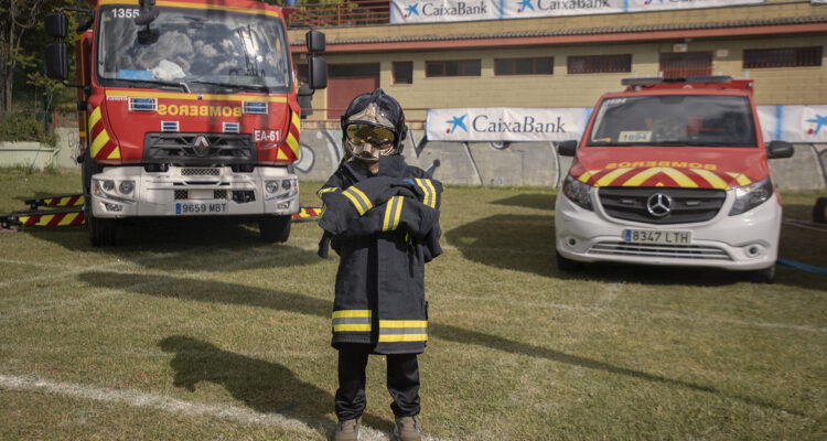 Niño vestido con un traje de bombero posa frente a varios vehículos