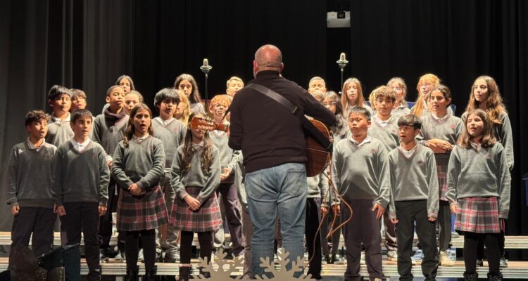 Coro del Colegio Virgen del Pilar, clasificados con el segundo puesto, donde aparece el profesor tocando la guitarra en el escenario frente a los niños