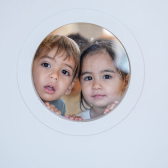 Alumnos de la Escuela Infantil Municipal Muñeco de Nieve se asoman por el cristal de una puerta blanca