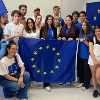 Grupo de jóvenes participantes del programa Europa Joven posando con banderas de la Unión Europea en un aula, sonriendo a la cámara