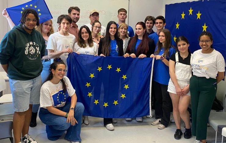 Grupo de jóvenes participantes del programa Europa Joven posando con banderas de la Unión Europea en un aula, sonriendo a la cámara