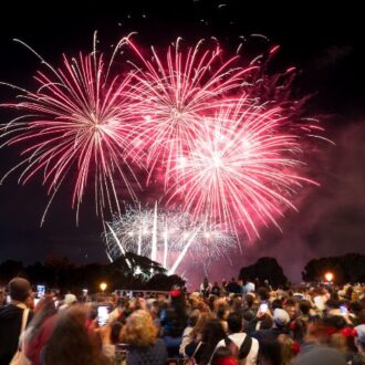Fuegos artificiales iluminan el cielo nocturno mientras una multitud de personas observa y fotografía el espectáculo al aire libre durante una celebración festiva en Madrid