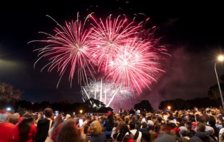 Fuegos artificiales iluminan el cielo nocturno mientras una multitud de personas observa y fotografía el espectáculo al aire libre durante una celebración festiva en Madrid